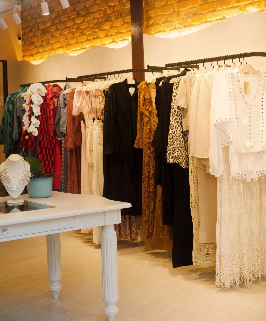 Interior da Branca Boutique Coffee Itaipava com arara colorida de roupas femininas e mesa de vitrine